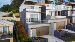 A modern residential building with multiple levels, large windows, and a balcony. - Brand new house, amazing views, walk to the beach! (Kiama)
