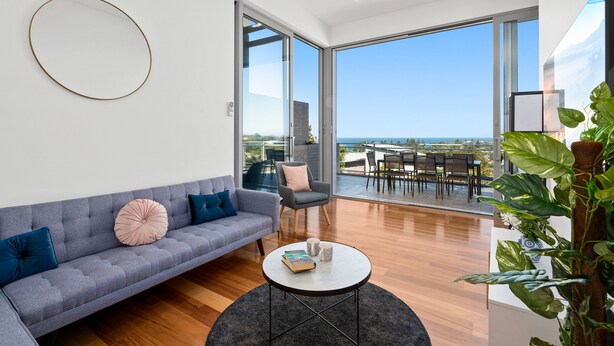 A modern living room with a grey sofa, a round coffee table, and a large window offering a view of the ocean. - Brand new house, amazing views, walk to the beach! (Kiama)