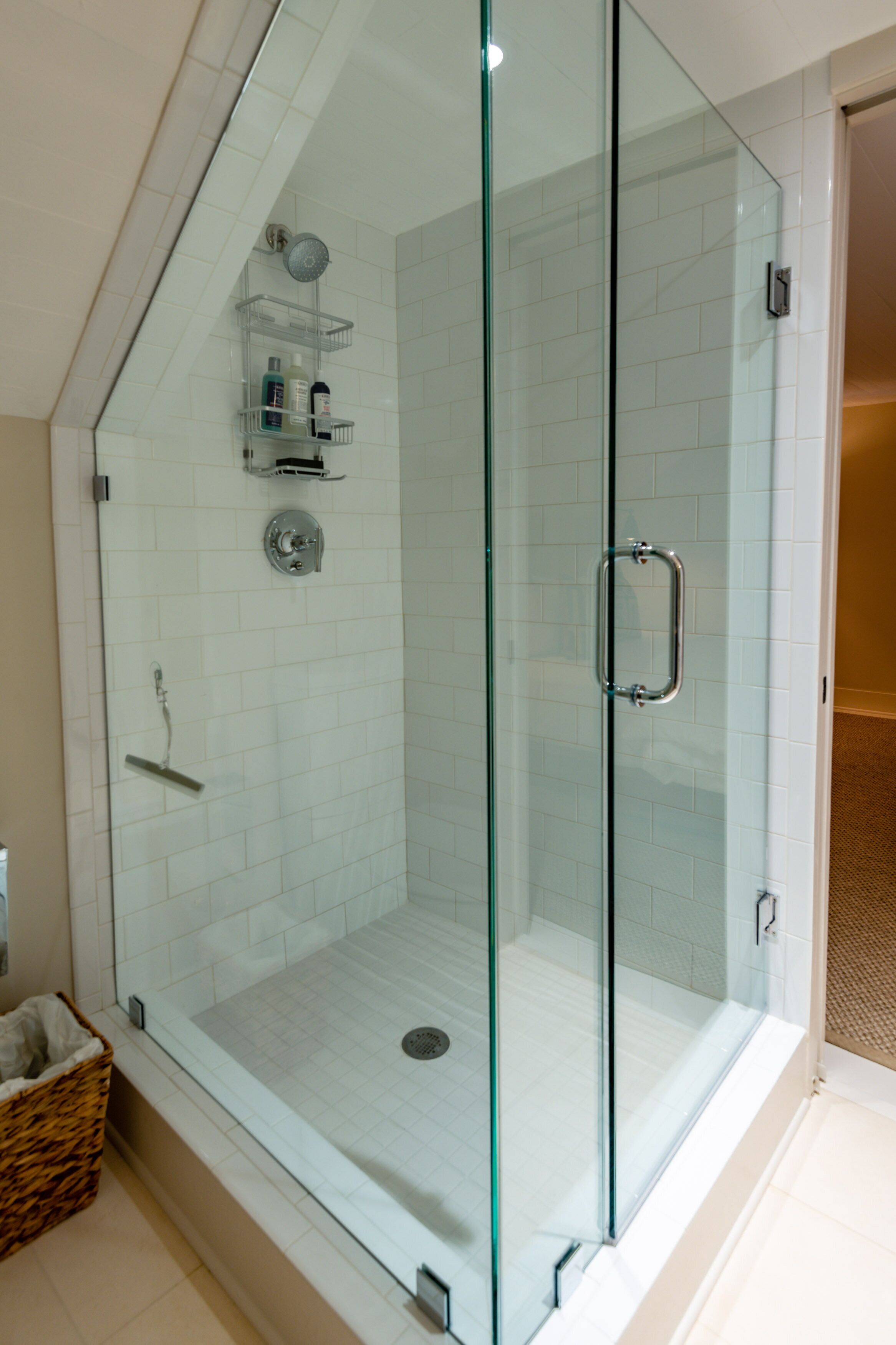 A glass-enclosed shower with a glass door, a metal handle, and a shelf with toiletries.