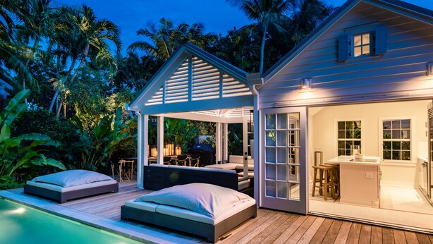 Et moderne hus med en pool, et overdækket udeområde og et køkken, der kan ses gennem den åbne dør.
