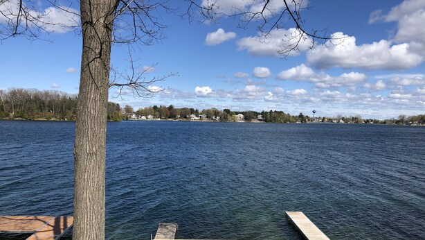 A wooden dock extending into a calm lake with a clear sky and distant houses. - Silver Lake Cabin (Traverse City)