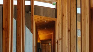 A wooden interior corridor with a glass door on the right, a ceiling light, and a visible exit sign. - Large Black Butte Home With Private Hot Tub (Sisters)