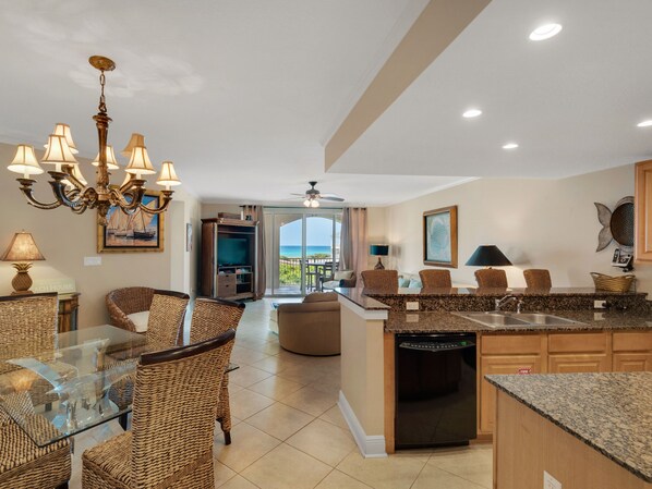 A spacious kitchen with a central island, dining area with wicker chairs, and a view to the outside.