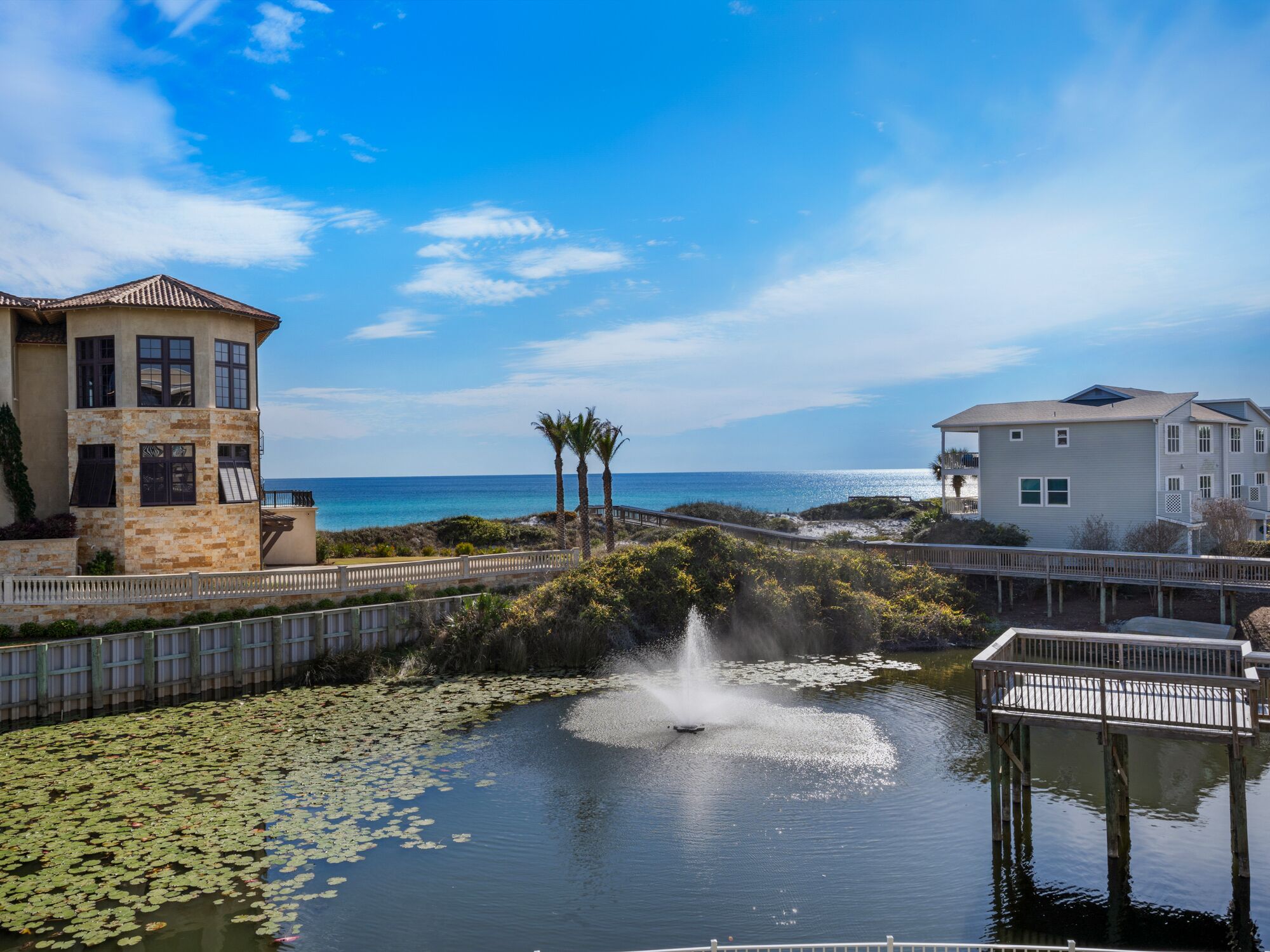 A waterfront property with a fountain, a pool with lily pads, and two buildings with balconies overlooking the water.