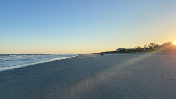 A wide, empty beach with a clear sky and a building in the background.