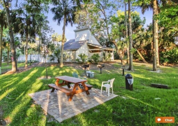 A house with a patio area featuring a picnic table and chairs, surrounded by trees.