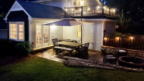 Et toetagers hus med balkon, terrasse med udendørs møbler og en godt oplyst indgang.