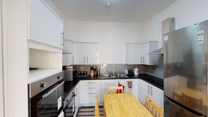 Una cucina compatta con mobili bianchi, un frigorifero in acciaio inossidabile, un tavolo da pranzo in legno e un forno integrato.