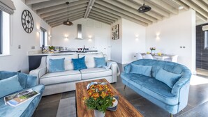 Ein modernes Wohnzimmer mit einer Couch, einem Couchtisch mit Blumen und einer Küche im Hintergrund.