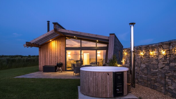 Ein modernes Haus mit Whirlpool, Sitzgelegenheit im Freien und einer Steinmauer.
