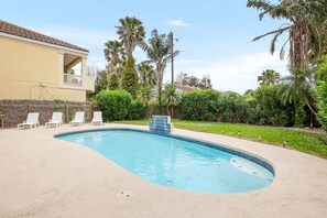 Une piscine dont le bord est recouvert de carrelage, entourée d’une terrasse beige et de chaises longues blanches.