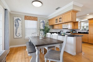 Un coin repas avec une table et des chaises en bois, une cuisine avec des placards en bois et une œuvre d’art représentant un hippocampe accrochée au mur.