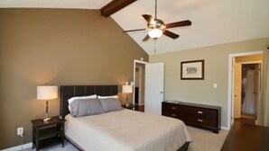 Un dormitorio con cama, lámparas de noche, cómoda, ventilador de techo y una puerta que da a otra habitación.