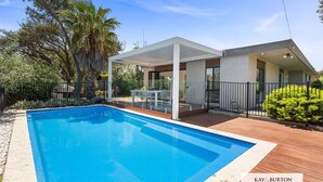 A modern pool area with a covered patio, a wooden deck, and a clear blue pool.
