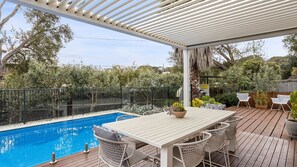 A covered outdoor area with a pool, a dining table with chairs, and a pergola.