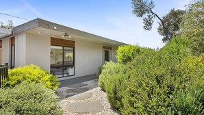 A modern house with a large glass window, a stone pathway, and lush greenery.