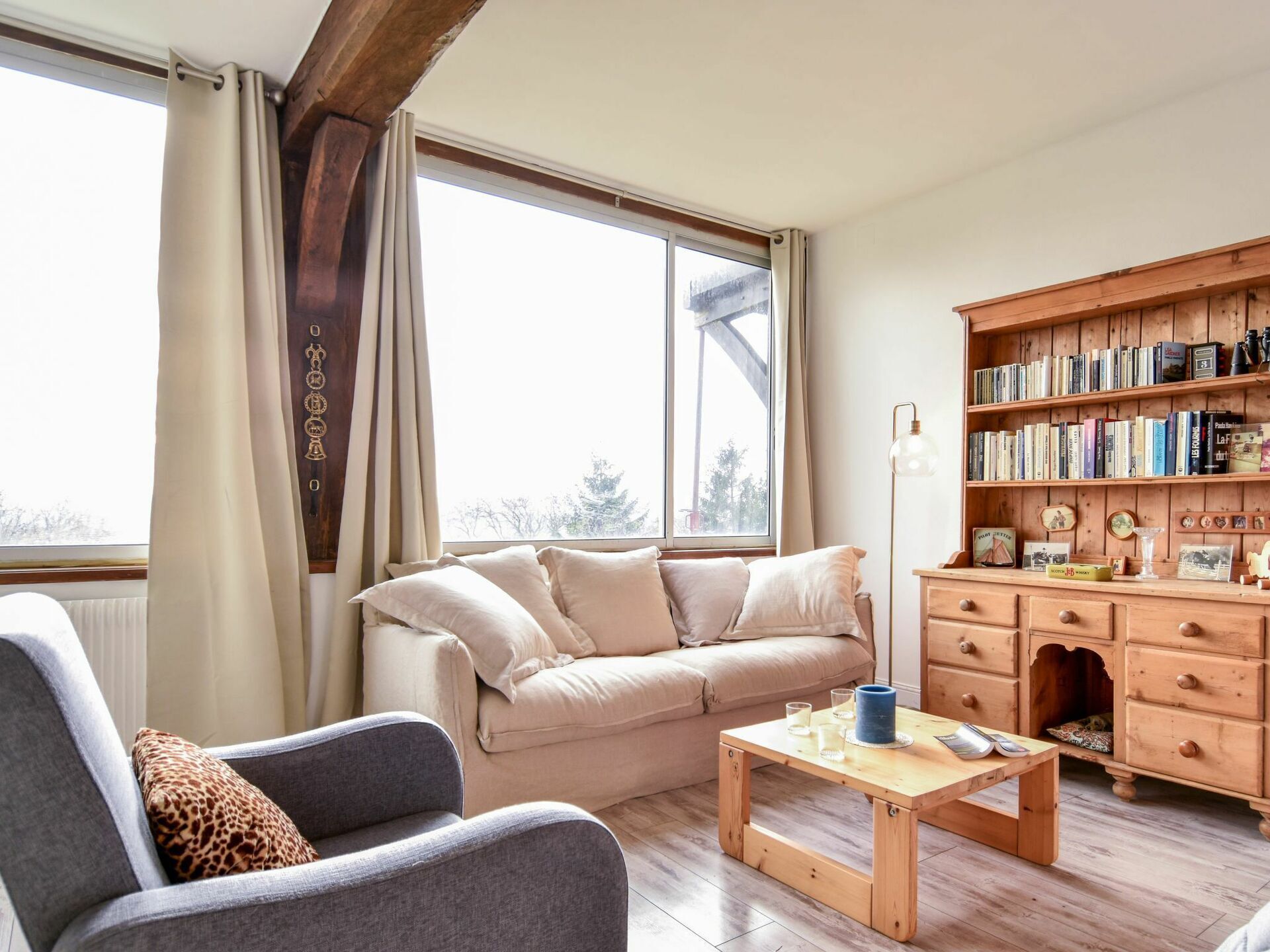 A cozy living room with a sofa, armchair, wooden coffee table, and a bookshelf filled with books.