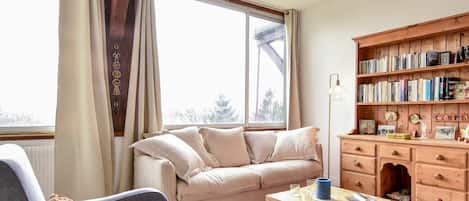 A cozy living room with a sofa, armchair, wooden coffee table, and a bookshelf filled with books.