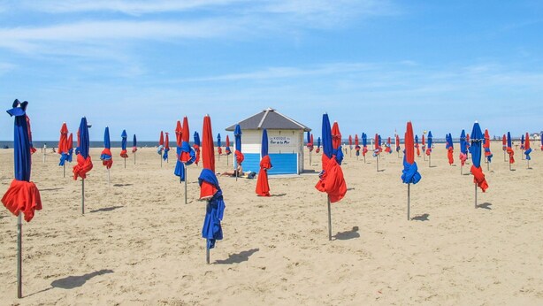 A beach with rows of red and blue umbrellas, a lifeguard hut, and a sandy beach. - Nice apartment for 3 guests with WIFI, TV and panoramic view (Tourgeville)