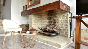 A cozy living room with a stone fireplace, a white chair, a small round table, and a TV on a wooden stand. - Nice apartment for 3 guests with WIFI, TV and panoramic view (Tourgeville)