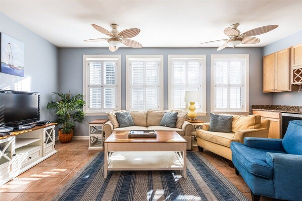 Ein Wohnzimmer mit einer Couch, einem Couchtisch, einem Fernseher und einem Deckenventilator.