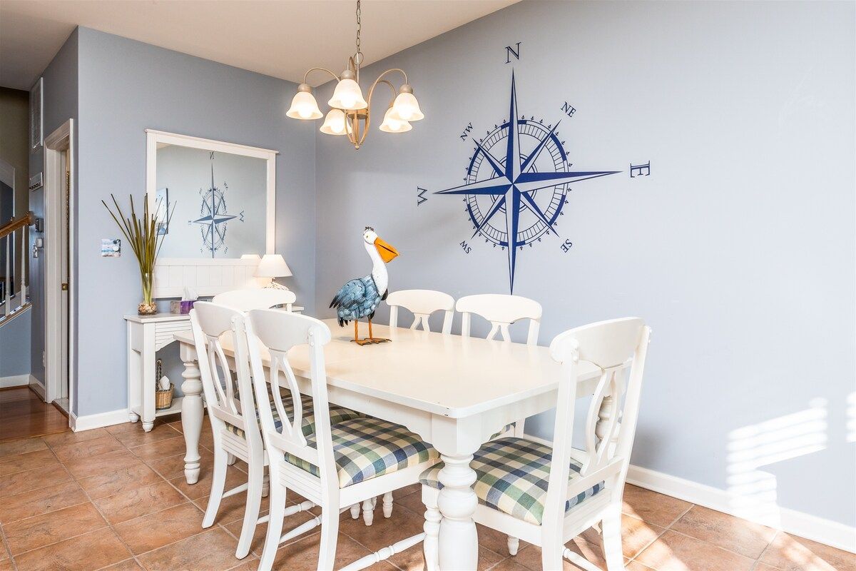 A dining area with a white table and chairs, a compass wall decoration, and a chandelier.