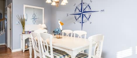A dining area with a white table and chairs, a compass wall decoration, and a chandelier.