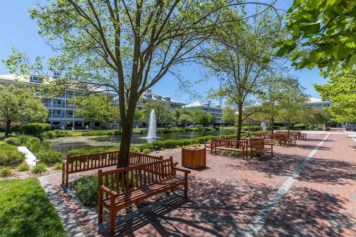A courtyard with benches, a fountain, and a pond, surrounded by trees and buildings.