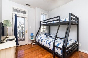 A bunk bed with a dolphin-themed bedspread, a desk with a lamp, and a window with a view of trees.