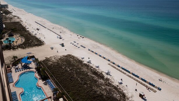 An aerial view of a beach resort with a swimming pool, beach chairs, and a pier in the background. - Great Weekly Rate With Beachfront Views (Panama City Beach)