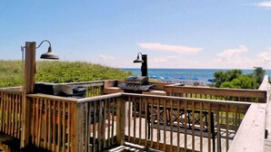 A wooden deck with barbecue grills and outdoor lighting, overlooking a beach with umbrellas and the ocean. - Great Weekly Rate With Beachfront Views (Panama City Beach)