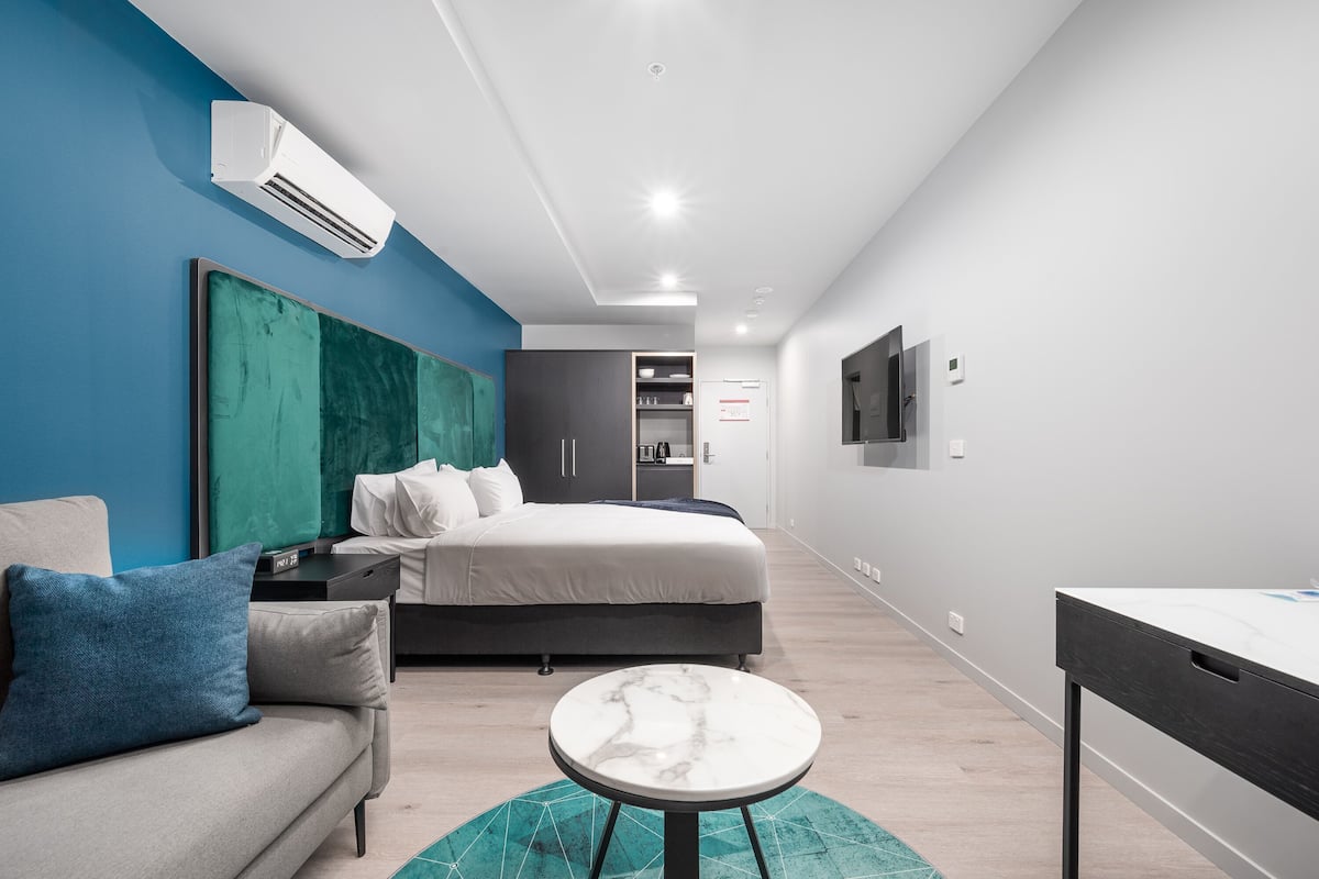 Una camera d'albergo moderna con un letto, un divano, un tavolino rotondo e una TV montata a parete.