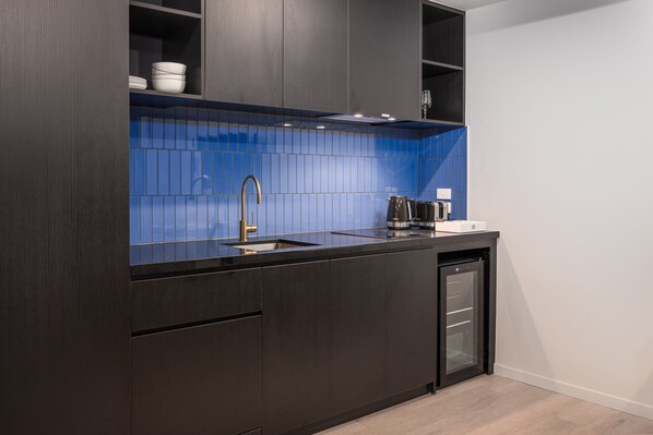 A modern kitchen with dark cabinetry, a blue tiled backsplash, and a built-in dishwasher.