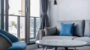 Ein modernes Wohnzimmer mit einem grauen Sofa, blauen Kissen, einem runden Marmor-Couchtisch und einem großen Fenster mit Vorhängen.