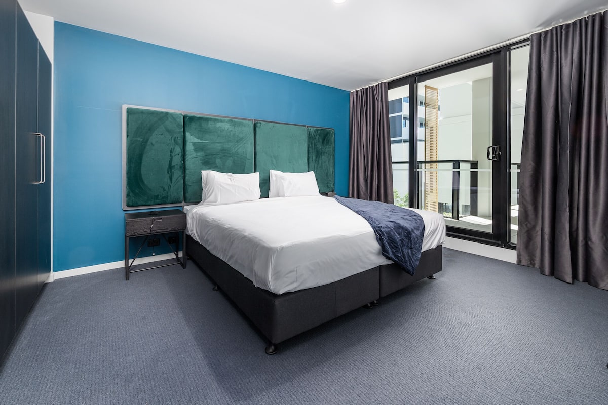 Una camera d'albergo moderna con un letto grande, un comodino, una scrivania e vista sull'esterno tramite una porta di vetro.
