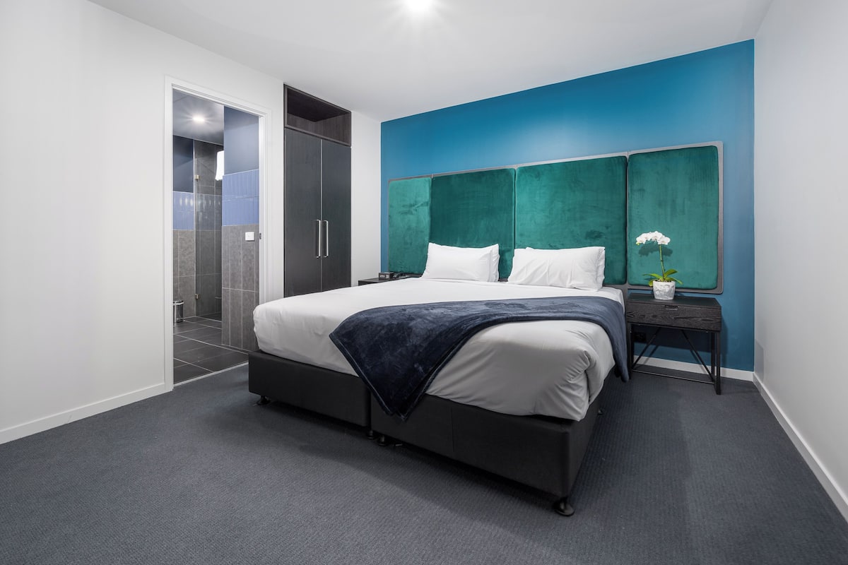 Camera da letto moderna con un letto grande, un comodino e una parete blu decorativa.