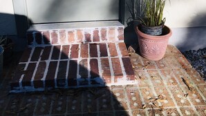 Eine Tür mit einer Metallklinke, einem Backsteinpodest und einem Blumentopf im Erdgeschoss.