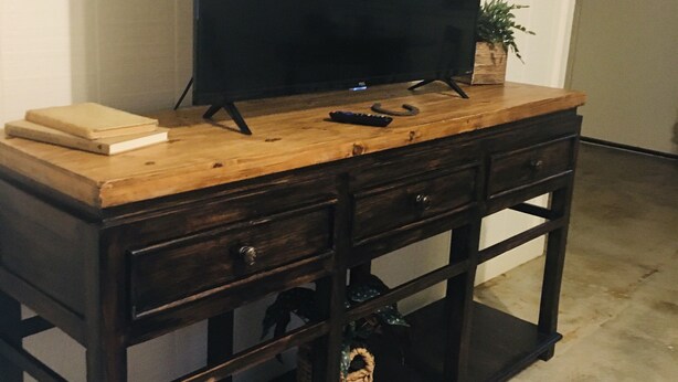 Ein Holz-Fernsehschrank mit Flachbildfernseher, Fernbedienung und einer kleinen Pflanze.