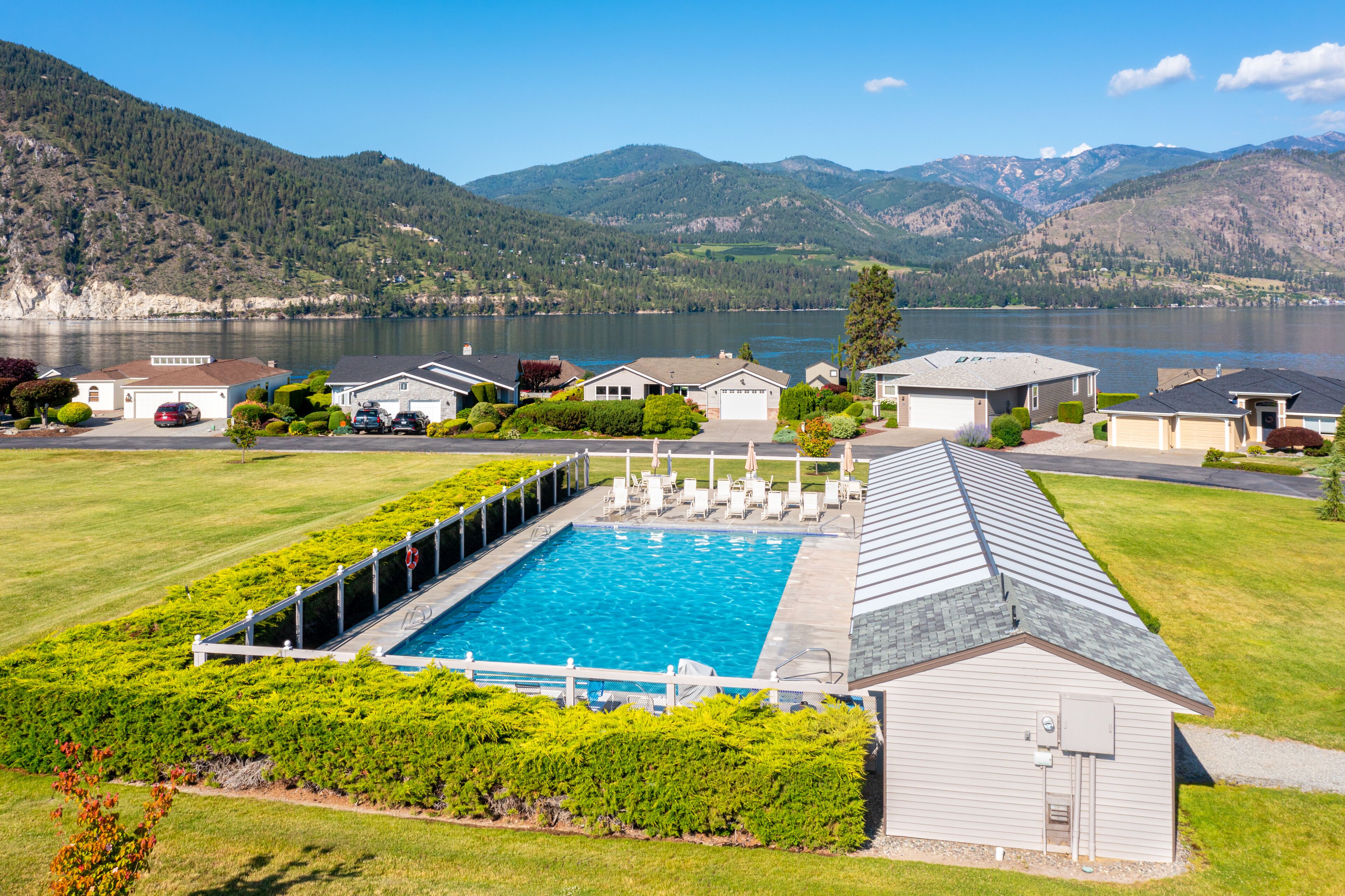 Un quartier résidentiel doté d’une piscine, de maisons et d’un lac, avec des montagnes en toile de fond.