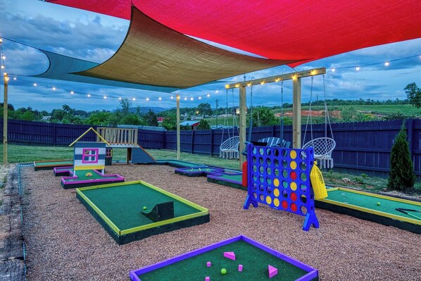 An outdoor play area with a swing set, a climbing structure, and a mini-golf setup.