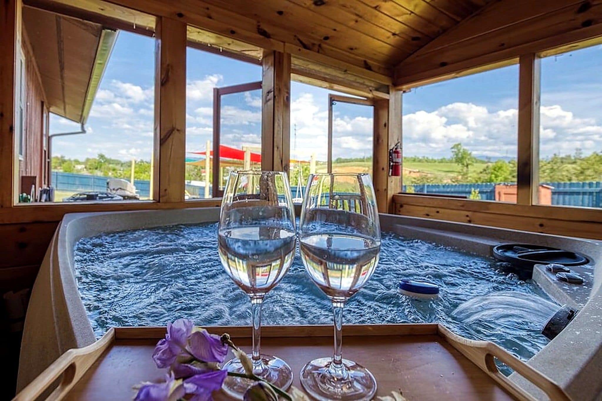 A hot tub with two glasses of water, a towel, and a flower on a wooden table.