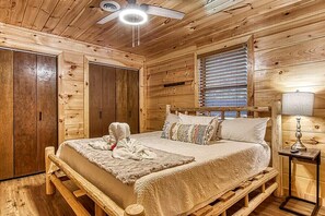 Un dormitorio de cabaña de madera con cama, mesita de noche, lámpara y ventilador de techo.