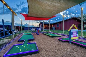 Un campo de mini golf al aire libre con una marquesina, una casita modelo y un columpio.