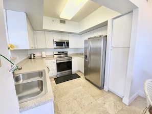 A modern kitchen with white cabinets, stainless steel appliances, a double sink, and a black mat.