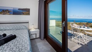 Een moderne hotelkamer met een bed, een nachtkastje, een lamp, een grote schuifglazen deur naar een buitenruimte met een tafel en stoelen, en twee ingelijste foto's aan de muur.