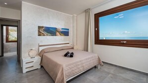 Een moderne slaapkamer met een bed, een nachtkastje, een raam met uitzicht op zee en een schilderij aan de muur.