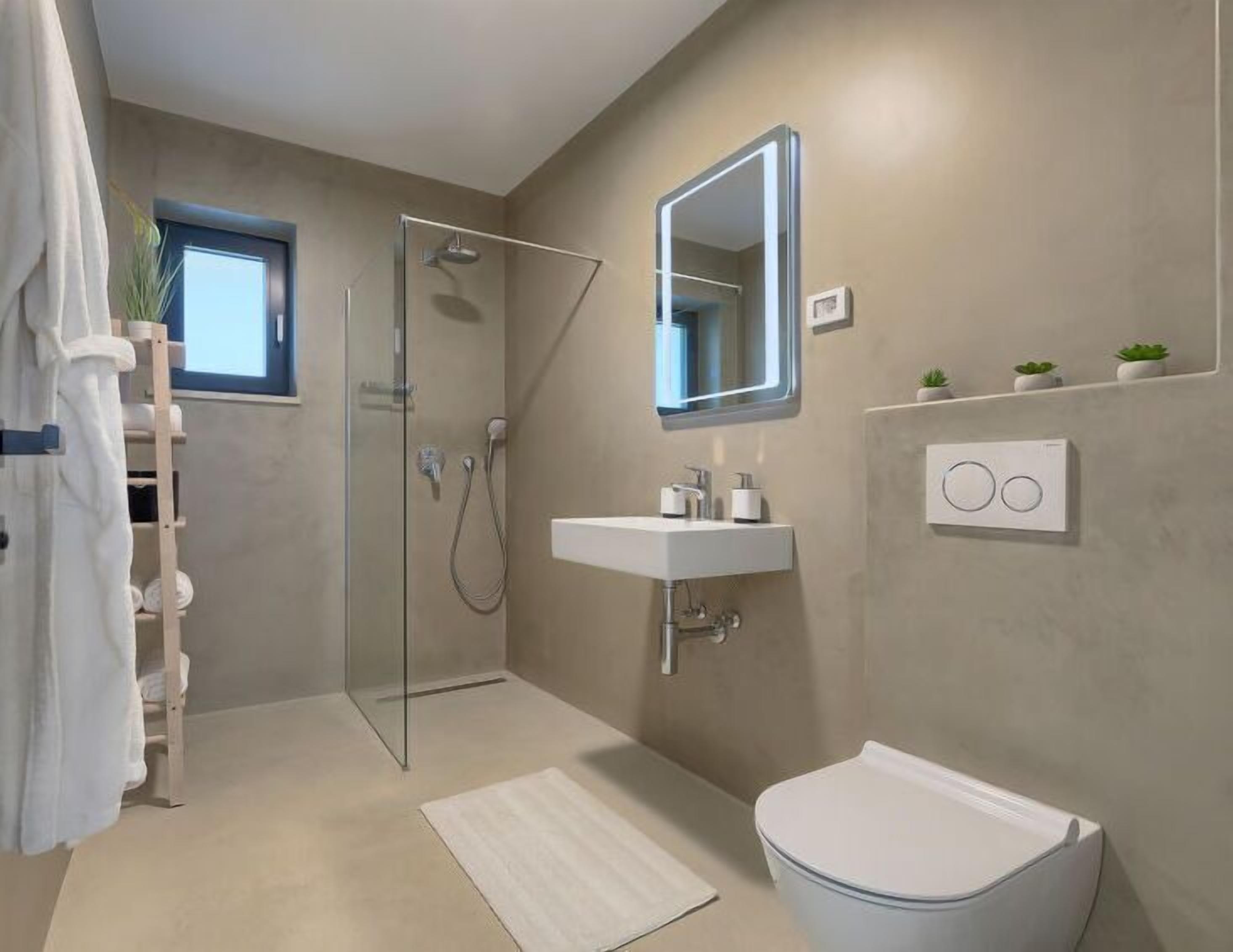 A modern bathroom with a glass shower enclosure, a white sink, a toilet, and a mirror.