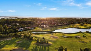 A golf course with sand bunkers, a pond, and a residential area in the background.