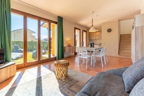 A spacious living area with a sofa, a dining table with chairs, a kitchen area, and a sliding glass door leading to a garden.