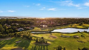 Campo de golf con búnkeres de arena, un estanque y una zona residencial al fondo.